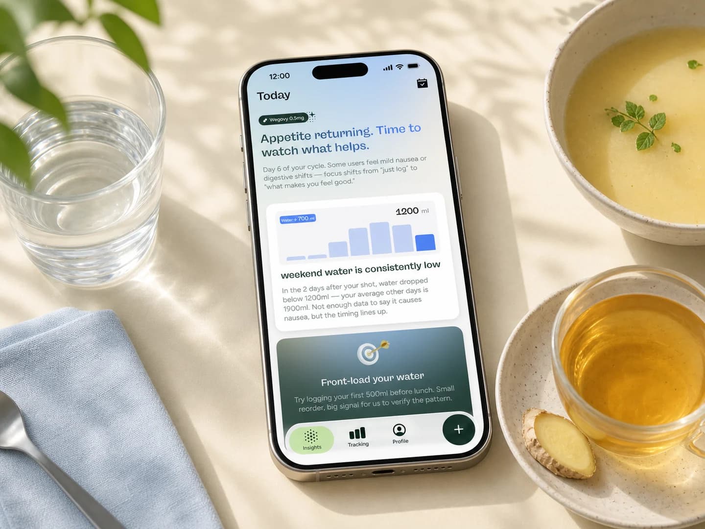 Phone showing a Glowise daily insight beside water, plain soup, ginger tea, and a pale blue napkin