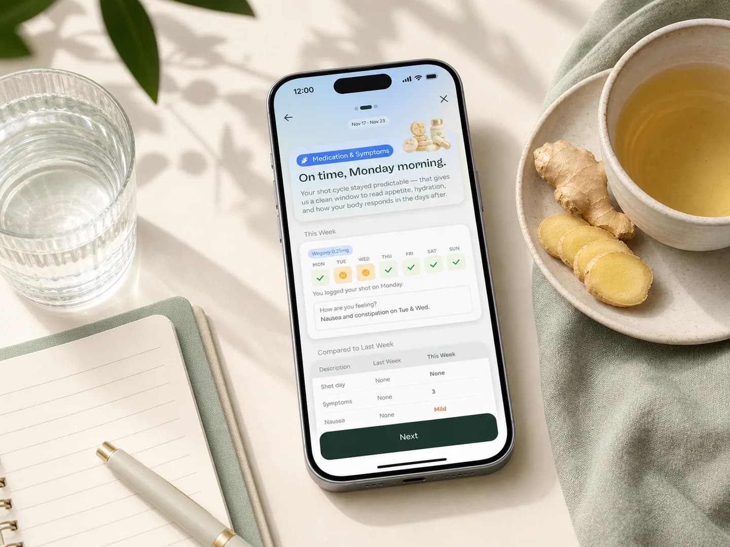 Phone showing a Glowise symptom check-in beside water, ginger tea, and a blank notebook