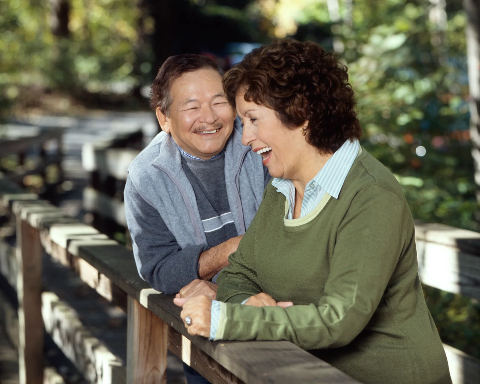 Two adults laughing together beside a wooden railing outdoors