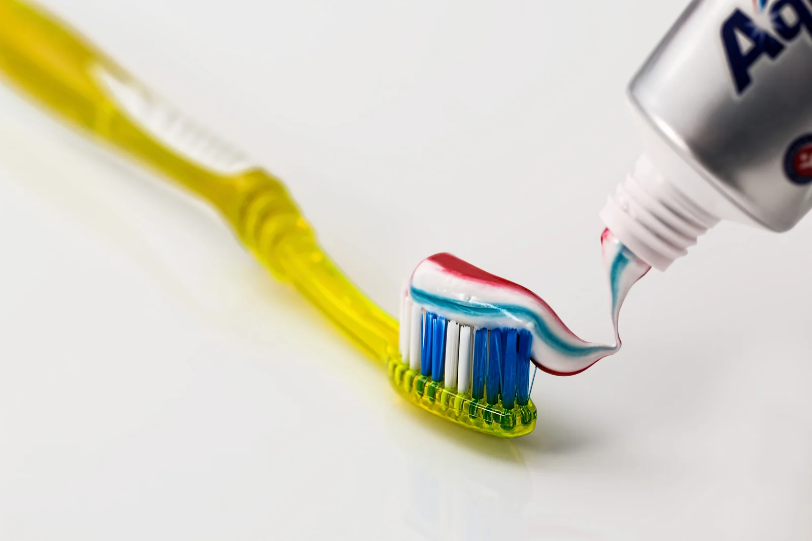 Toothpaste on a yellow toothbrush against a white background