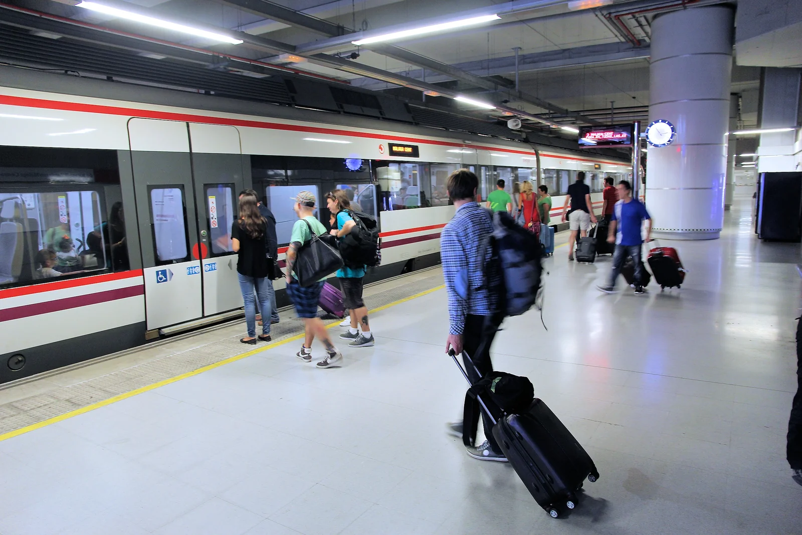 Travelers with rolling luggage beside a train at an airport rail station